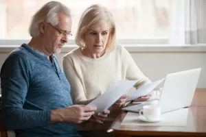 A husband and wife looking at documents in front of a laptop